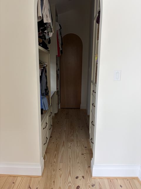 Walk-in closet with arched door and clean pine floors after a remodel cleanup