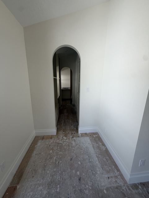 Arched hallway with drywall mud and paint splatter on the wood floor during a remodel